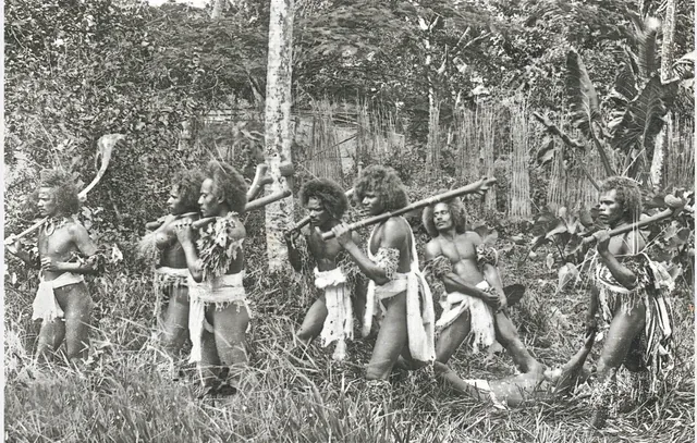 Original: Men carrying clubs, with a figure lying in the grass — early photograph, probably a staged scene (awaiting cultural review)
